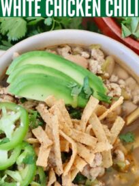 white chicken chili in bowl topped with tortilla strips, sliced jalapenos and avocado