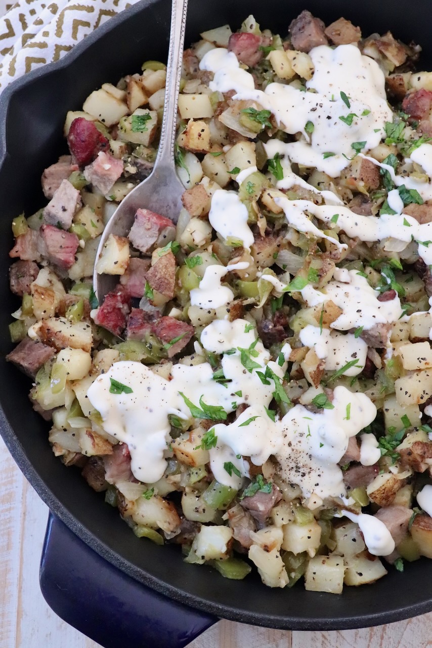 diced steak and potato hash in skillet, topped with cheese sauce