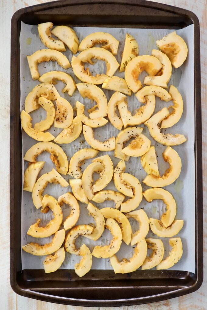 sliced pieces of delicata squash on baking sheet