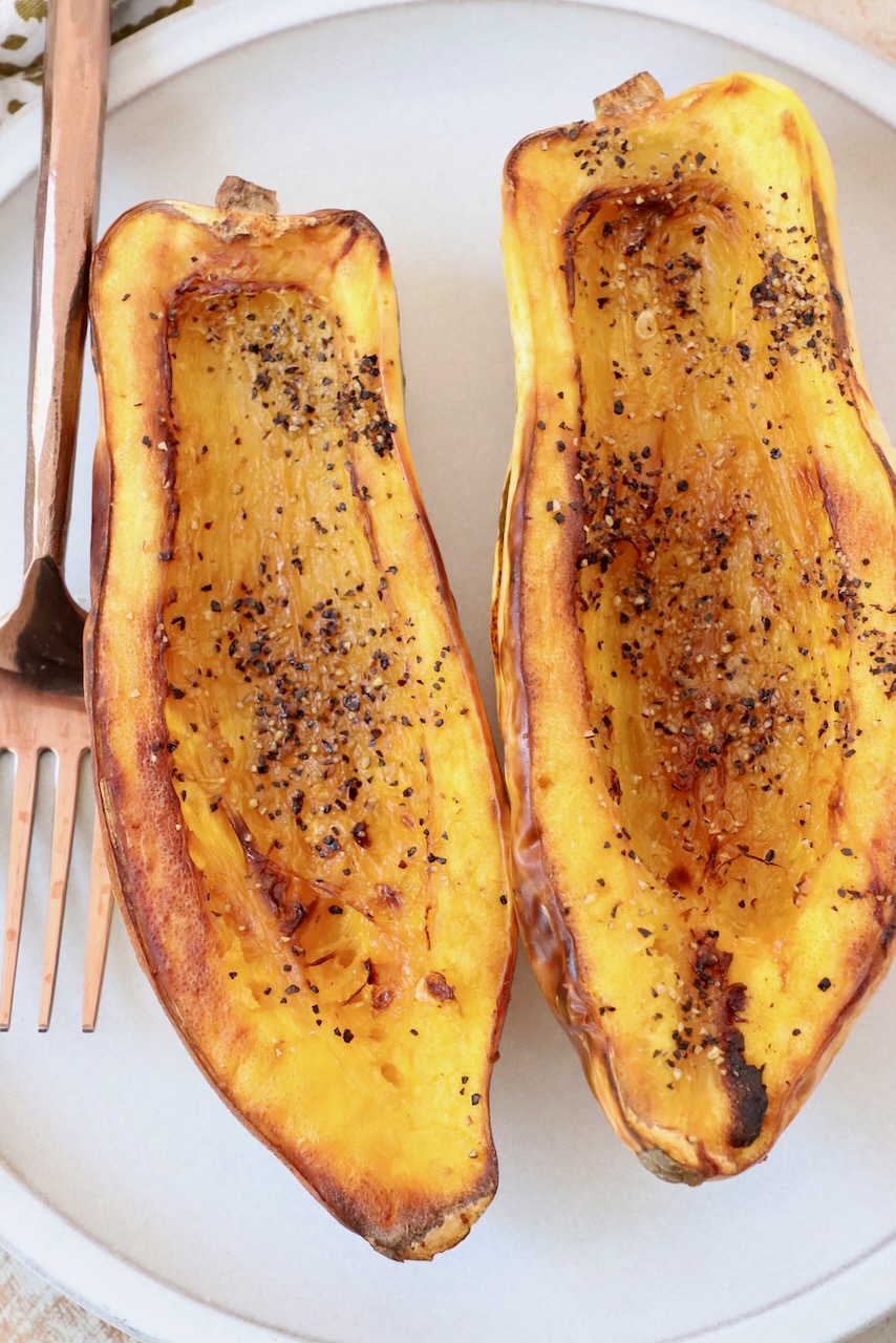 cooked delicata squash cut in half on plate with fork