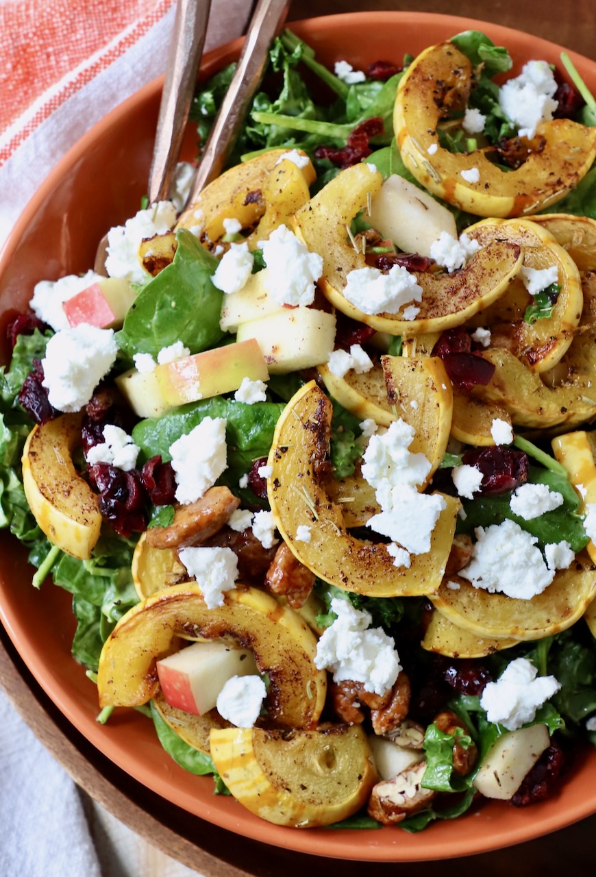 salad in bowl topped with roasted strips of delicata squash and crumbled goat cheese