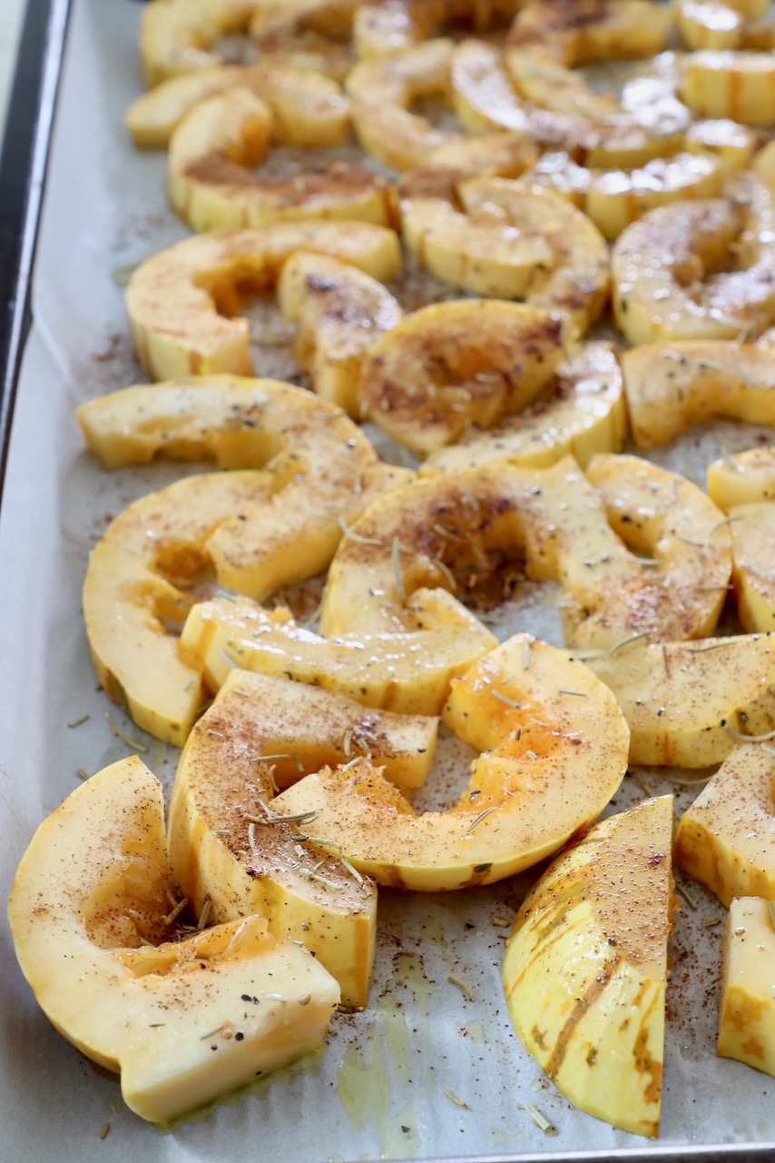 sliced seasoned delicata squash on baking sheet