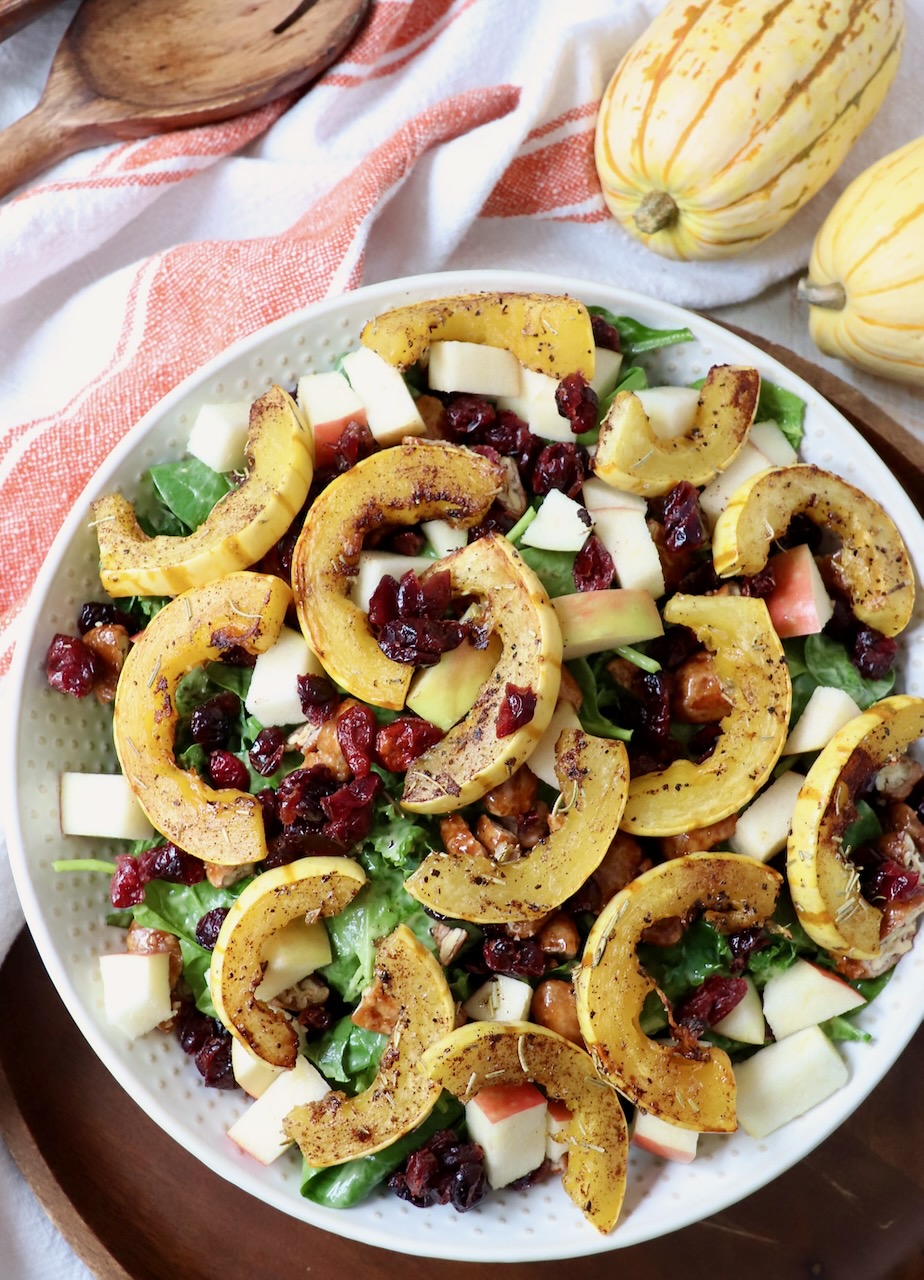 roasted slices of delicata squash on top of salad in large bowl
