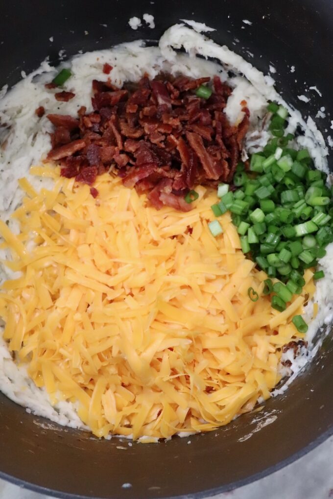 mashed potatoes in pot topped with shredded cheddar cheese, chopped cooked bacon and diced green onions