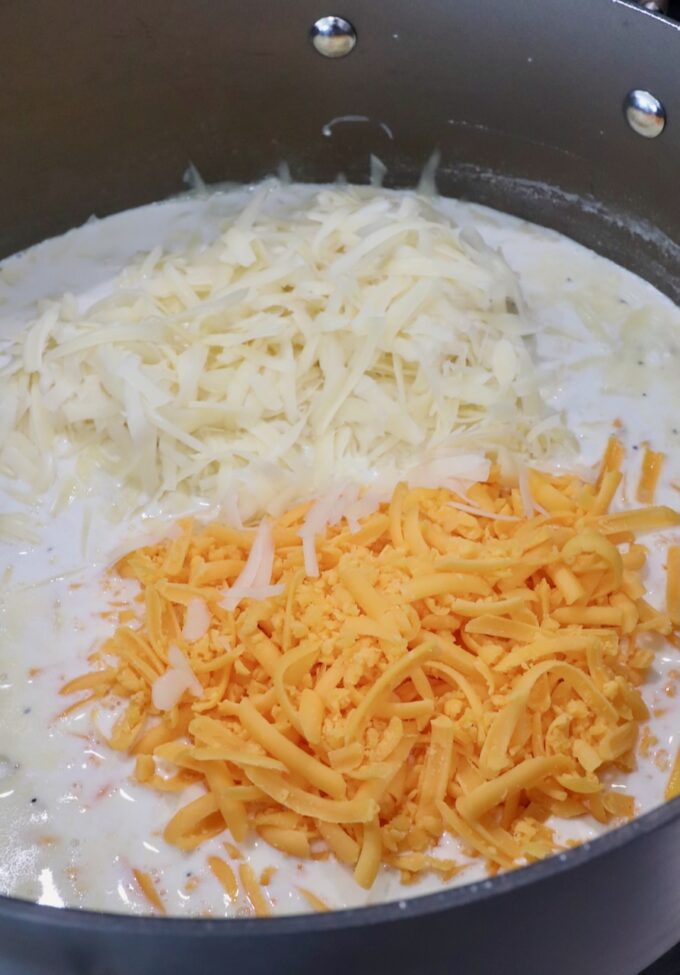creamy sauce in a large pot topped with shredded swiss and cheddar cheese