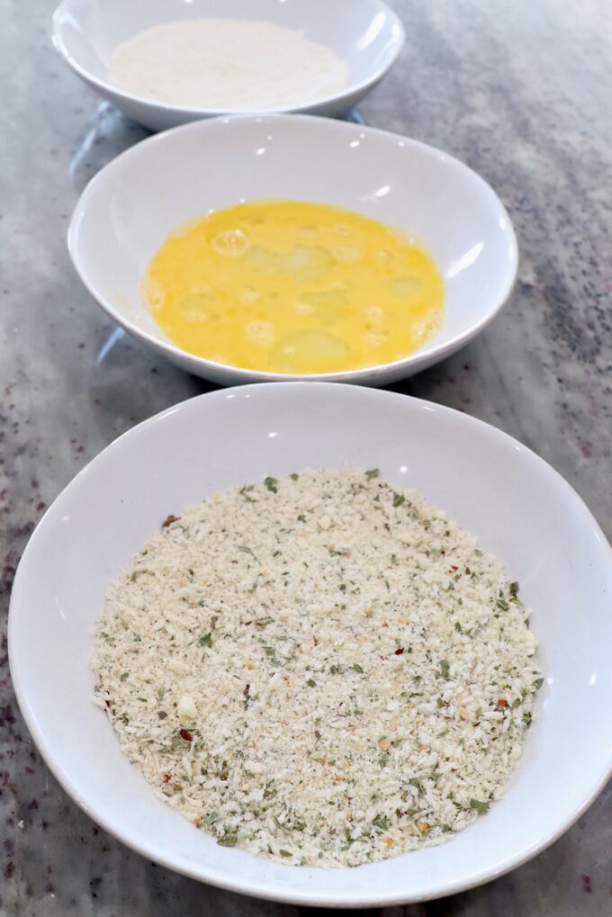 three bowls filled with breadcrumbs, whisked eggs and flour