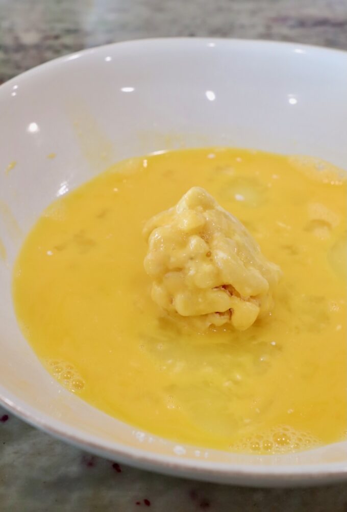 ball of mac and cheese rolled in whisked eggs in a shallow bowl