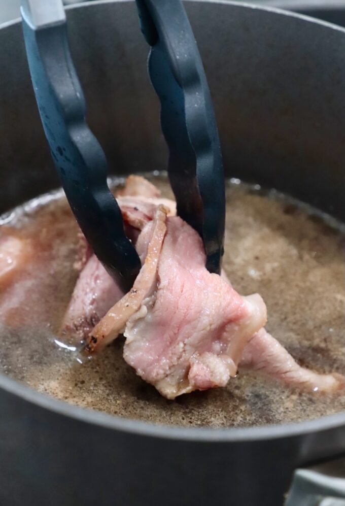 tongs holding beef in pot of boiling beef broth