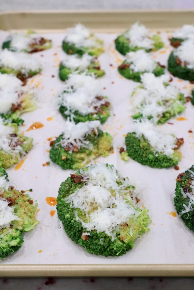 seasoned smashed broccoli on baking sheet topped with parmesan cheese