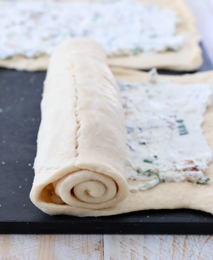 crescent roll dough rolled up over cream cheese filling on cutting board