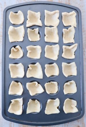 24 squares of crescent roll dough pressed into a mini muffin tin