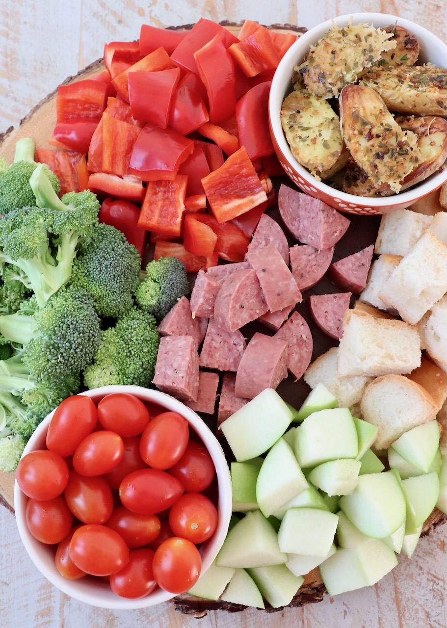 diced vegetables, apples, beef stick and cubes of bread on a wood tray
