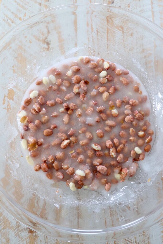 raw peanuts combined with corn syrup and sugar in a large glass bowl