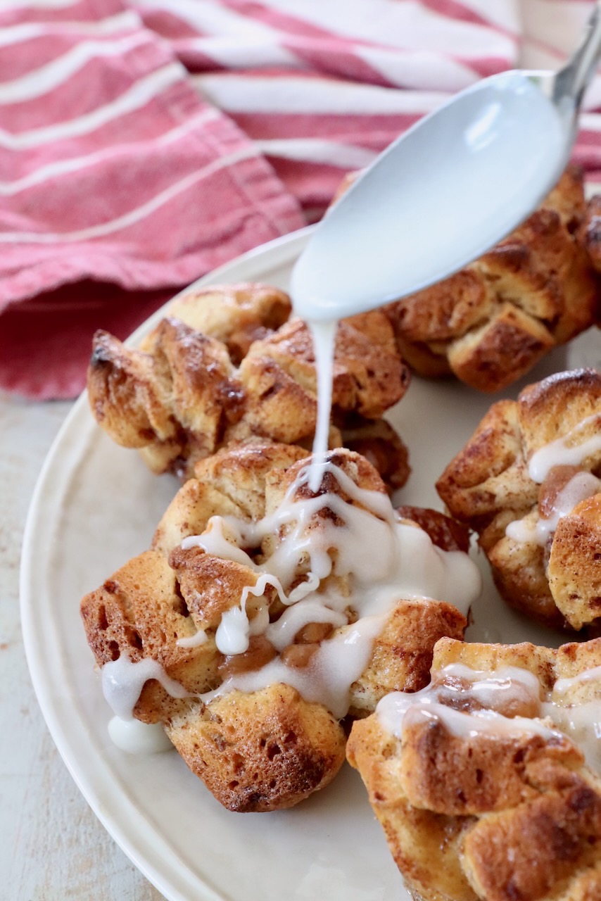cream cheese icing drizzled from spoon onto pull apart cinnamon rolls on a plate