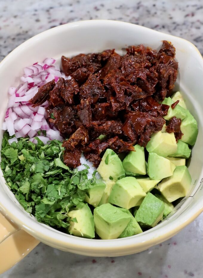 diced avocado, sun dried tomatoes, minced red onion and chopped cilantro in a bowl
