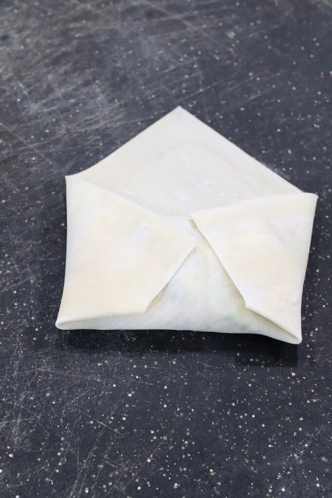 egg roll wrapper wrapped up over filling on a cutting board
