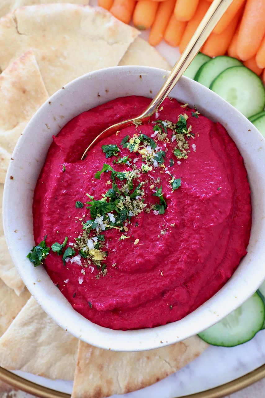 beet hummus in bowl with gold spoon