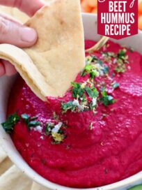 beet hummus in bowl with a piece of pita bread dipped into the hummus