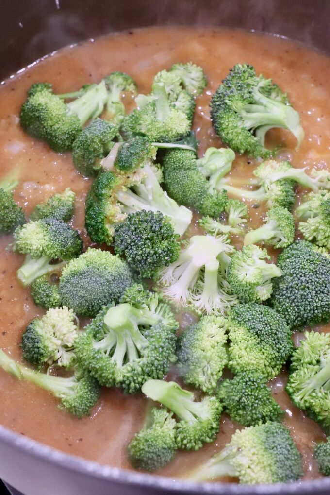 raw broccoli florets in pot with seasoned chicken broth