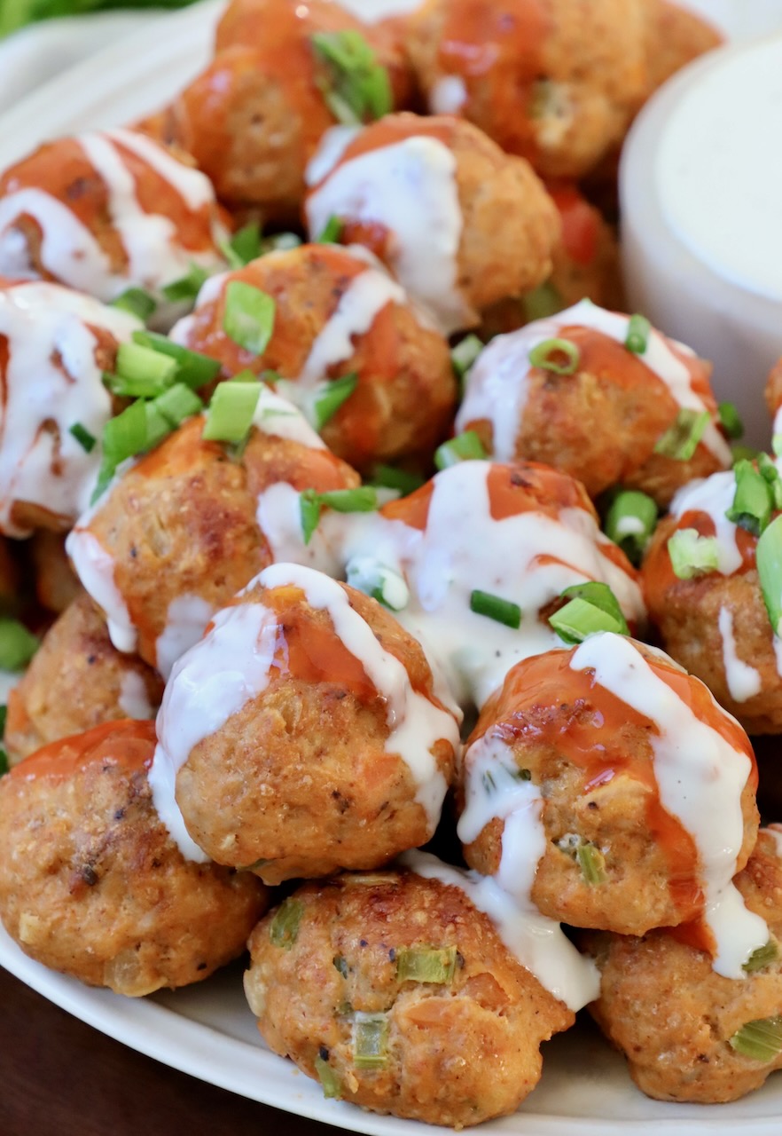 buffalo chicken meatballs stacked up on plate drizzled with blue cheese dressing and buffalo sauce