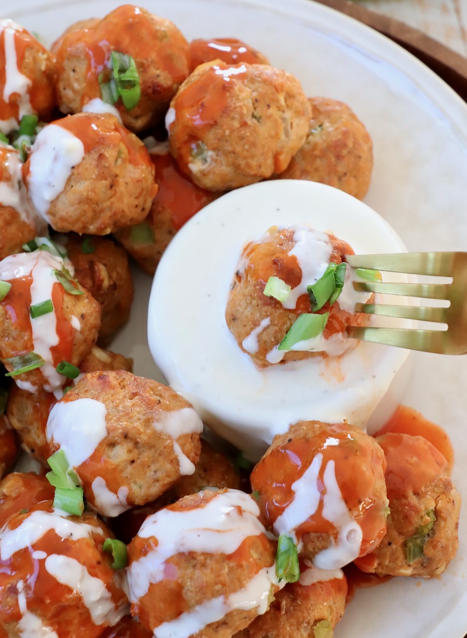 buffalo chicken meatball on fork, dipped into blue cheese dressing in a bowl