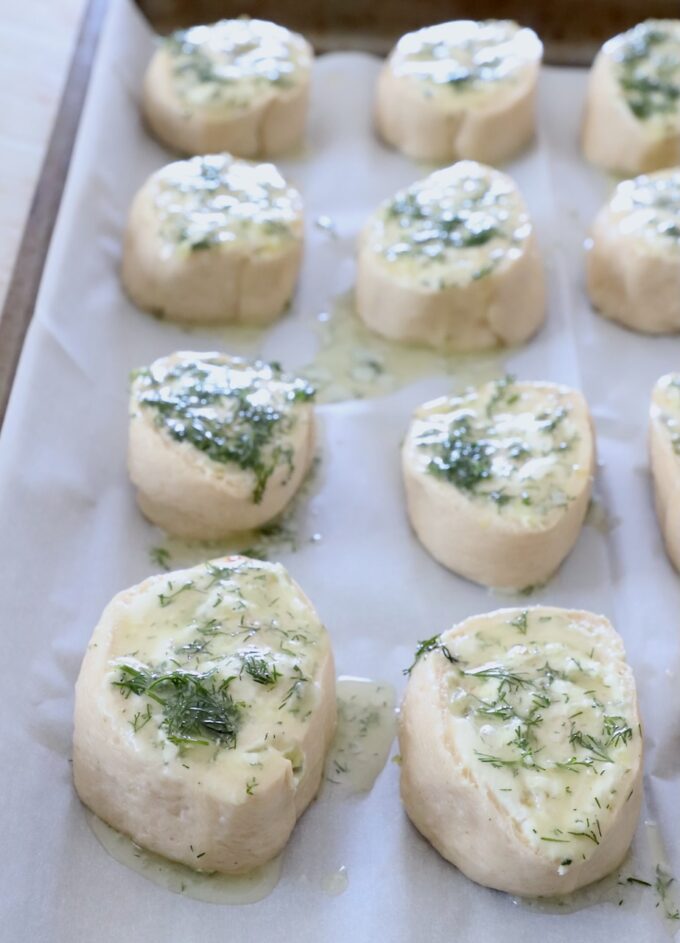 uncooked creamy pickle rolls on parchment-lined baking sheet topped with dill butter