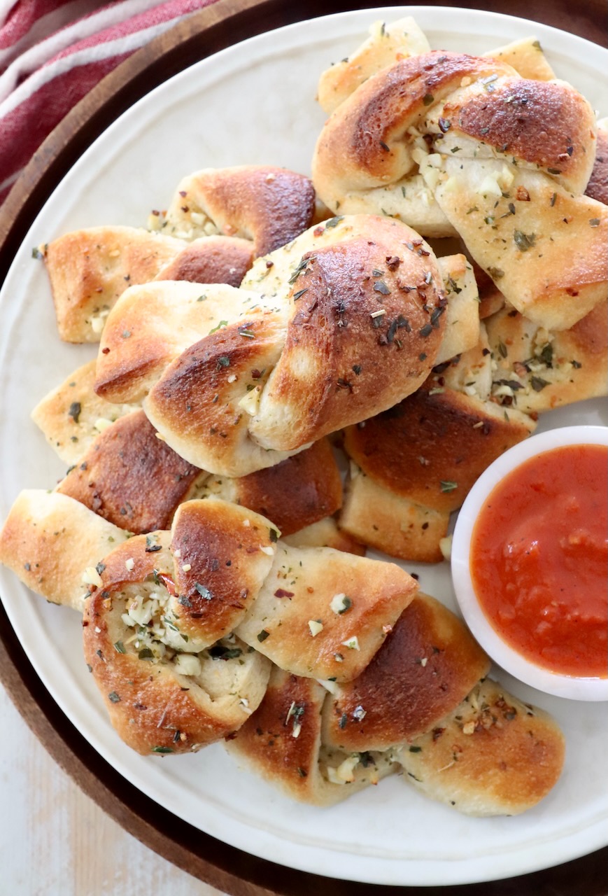 garlic knots stacked up on plate with a small bowl of marinara sauce