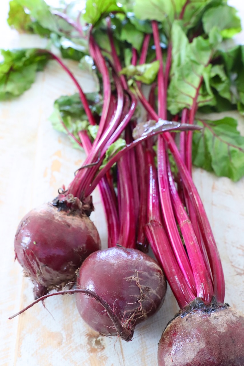 raw beets with the stems and greens attached on white wood board