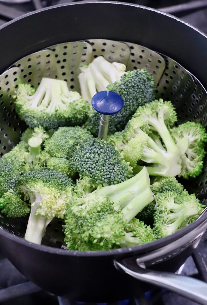 broccoli florets in steamer basket in pot on the stove