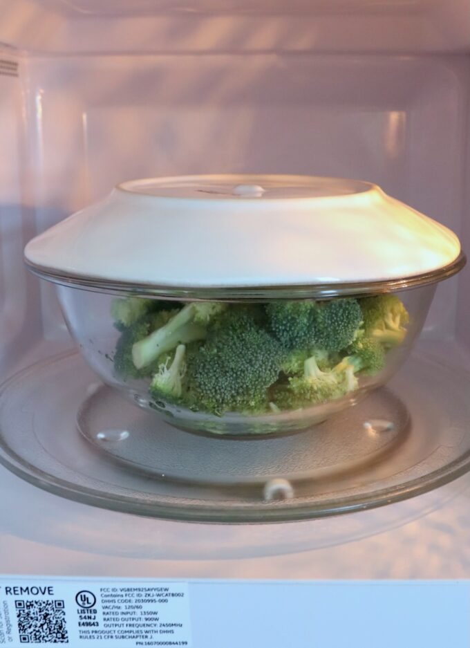 broccoli in bowl in microwave with a plate on top