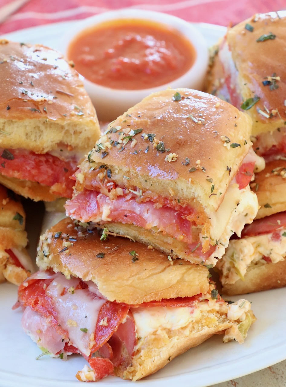 Italian sub sliders stacked up on a plate with a small bowl of marinara sauce on the side