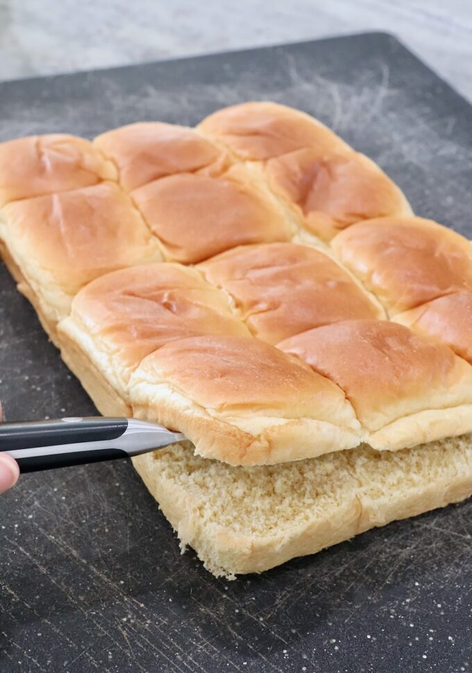 brioche rolls sliced through the middle with a knife on a cutting board
