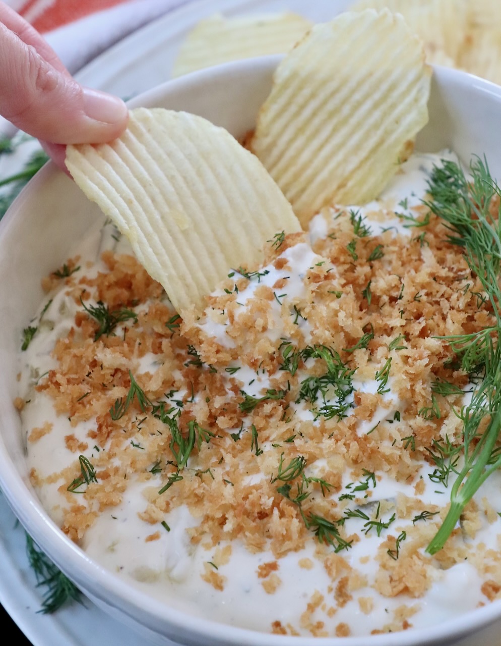 pickle dip in bowl topped with toasted breadcrumbs, with chip dipped into the bowl of dip