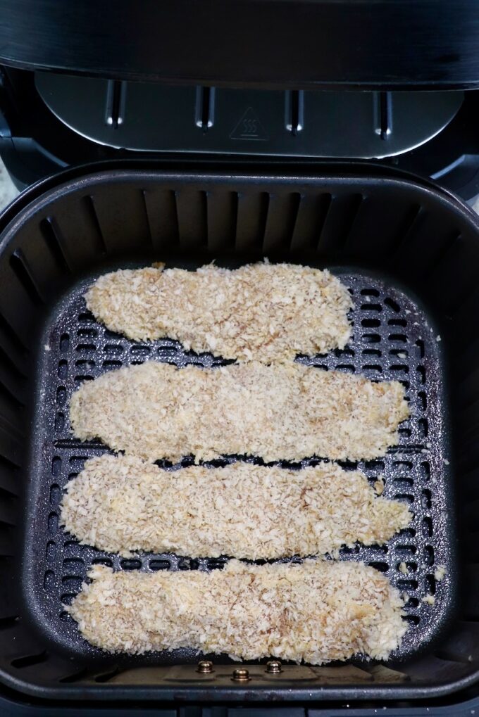 uncooked breaded chicken tenders in an air fryer basket