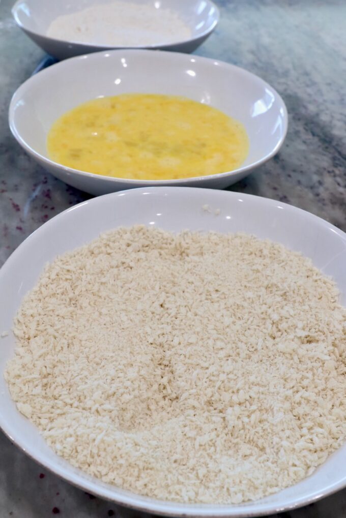 three bowls with breadcrumbs in one bowl, whisked eggs in another bowl and flour in the third bowl