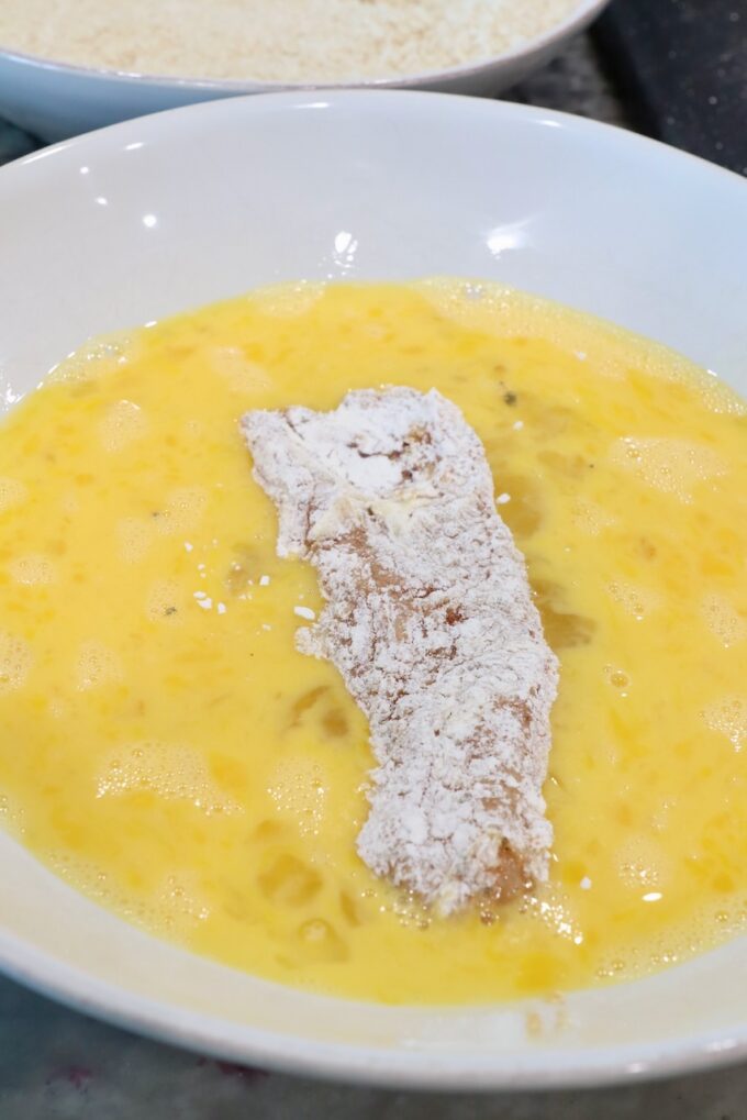 strip of seasoned flour-coated chicken in a bowl of whisked eggs