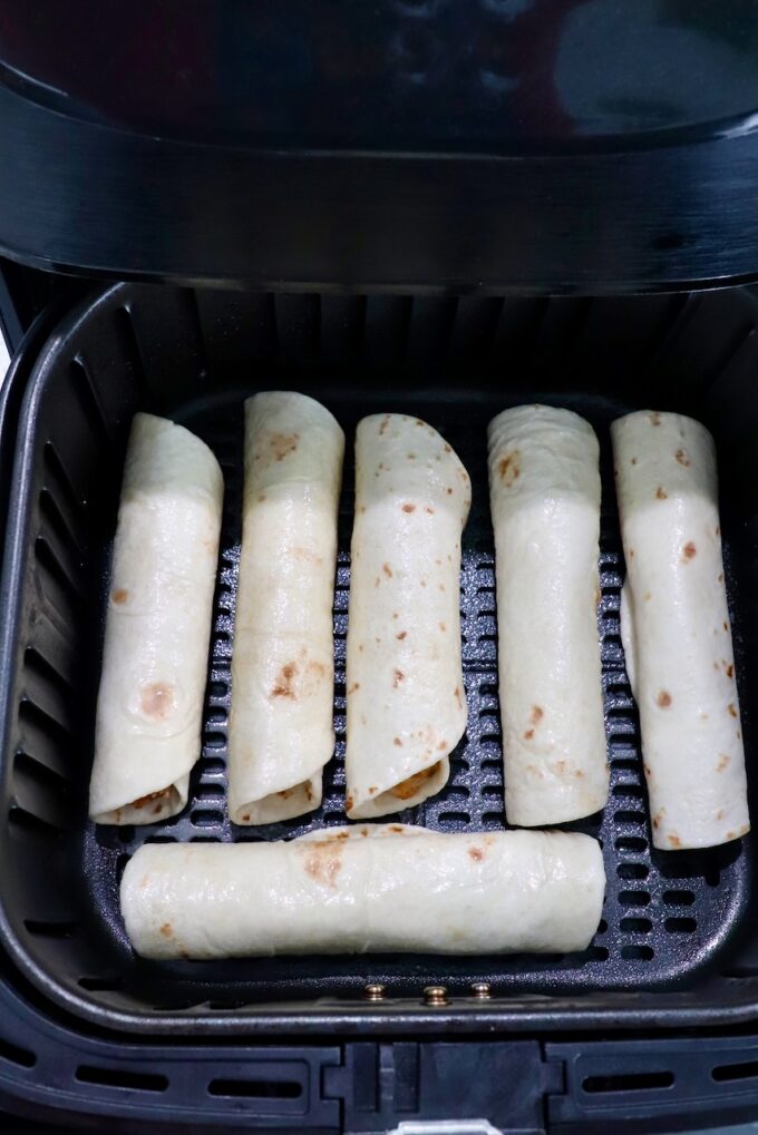 uncooked taquitos in an air fryer basket