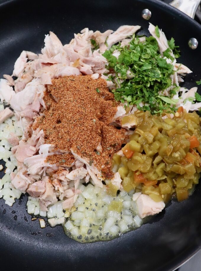 shredded chicken with diced onions, spices, cilantro and green chiles in a skillet