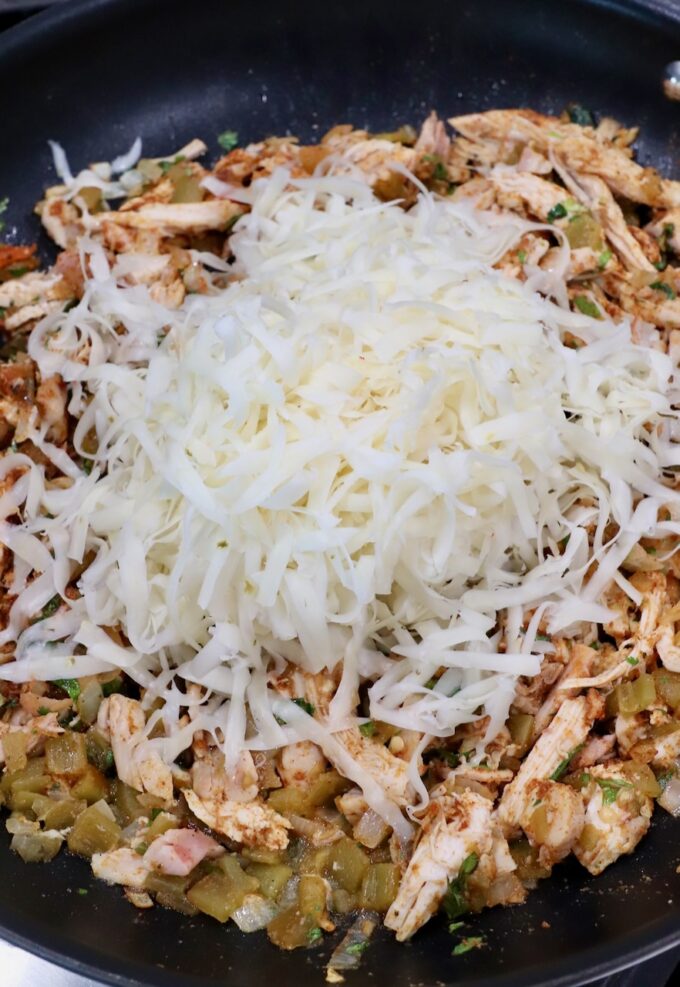 seasoned shredded chicken in skillet topped with shredded pepper jack cheese