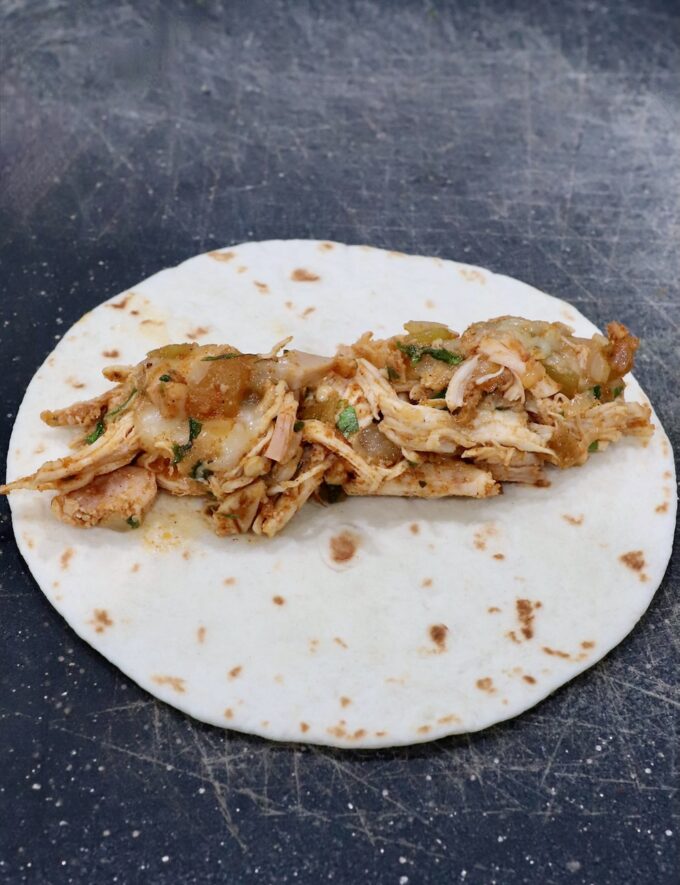 seasoned shredded chicken and cheese in the middle of a tortilla on a cutting board