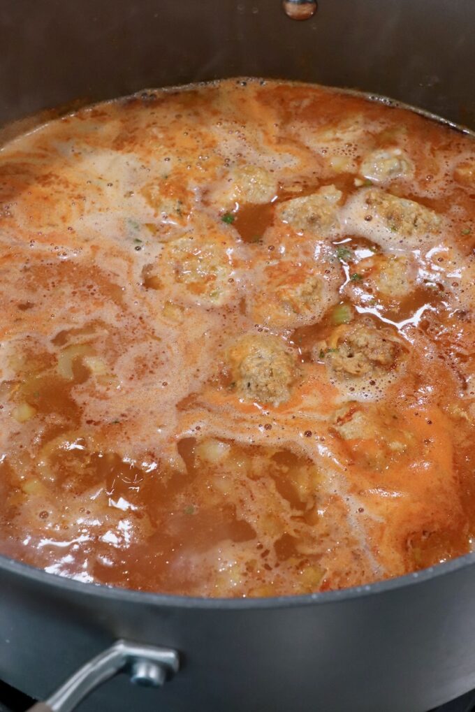 meatballs simmering in chicken broth seasoned with buffalo sauce in a large pot