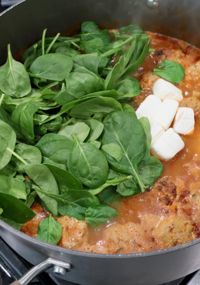 fresh spinach leaves and cubes of cream cheese in pot of buffalo chicken meatball soup