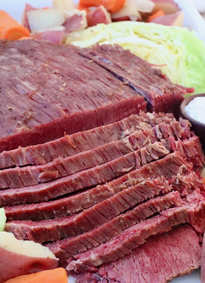 sliced corned beef on platter with cooked carrots, potatoes and cabbage