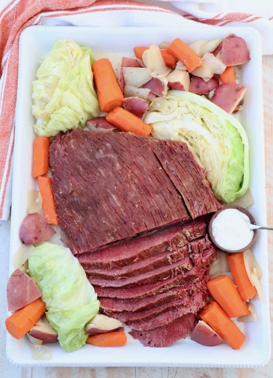 sliced corned beef on serving platter with cabbage, carrots, potatoes and onions