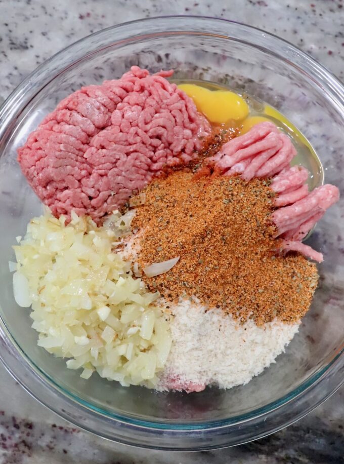 ground pork and beef in bowl with eggs, spices, cooked onions and breadcrumbs