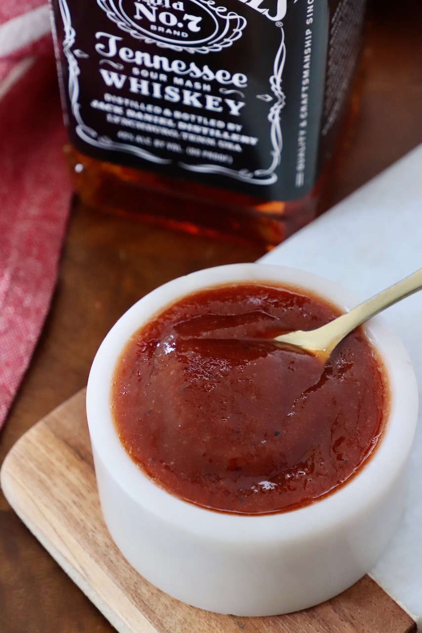bbq sauce in small bowl with spoon, with bottle of Jack Daniels whiskey behind it