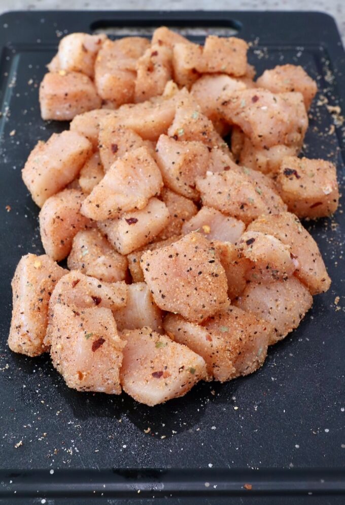 pieces of chicken breast meat tossed with seasoning on a cutting board