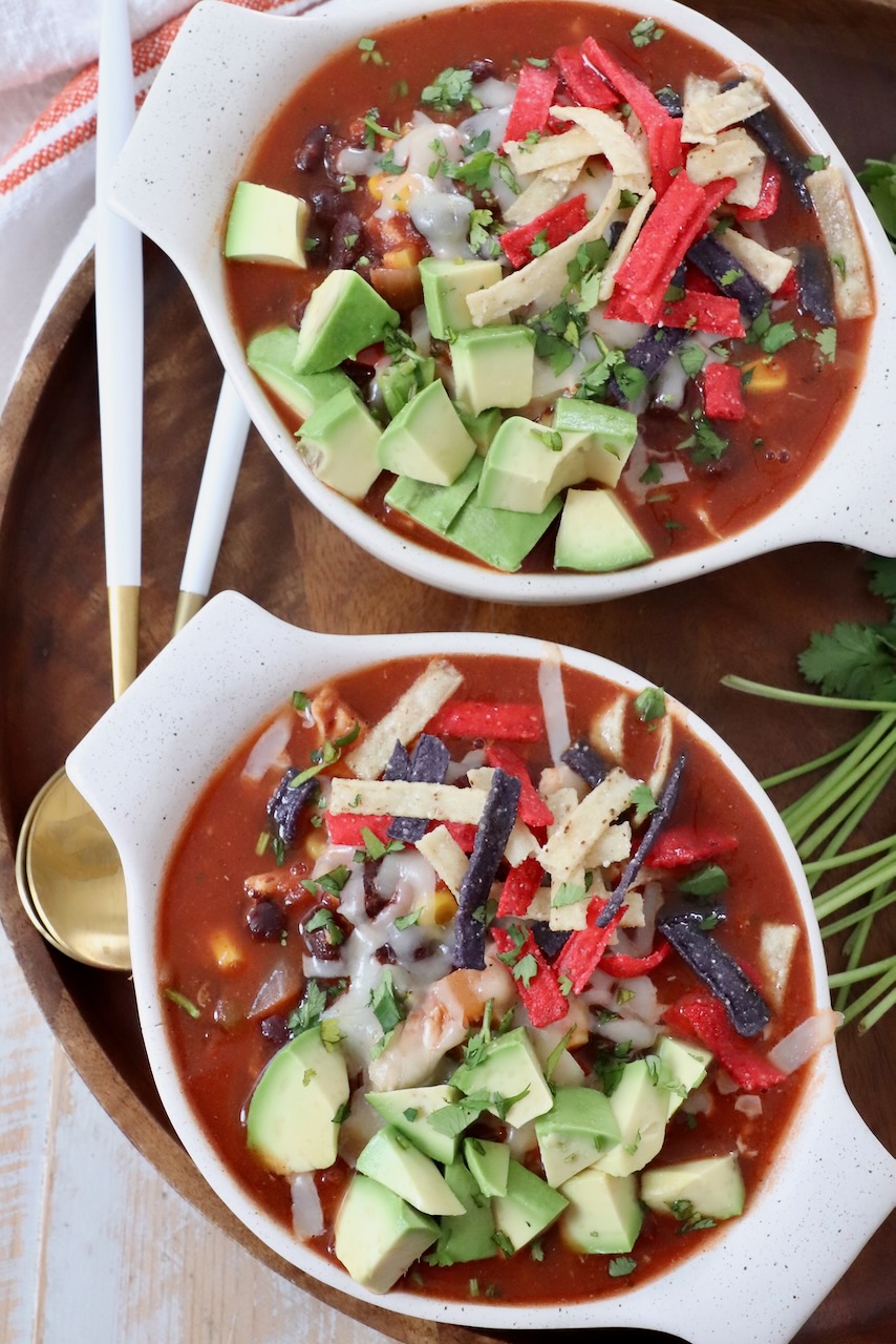 southwest chicken soup in two bowls topped with tortilla strips and diced avocado