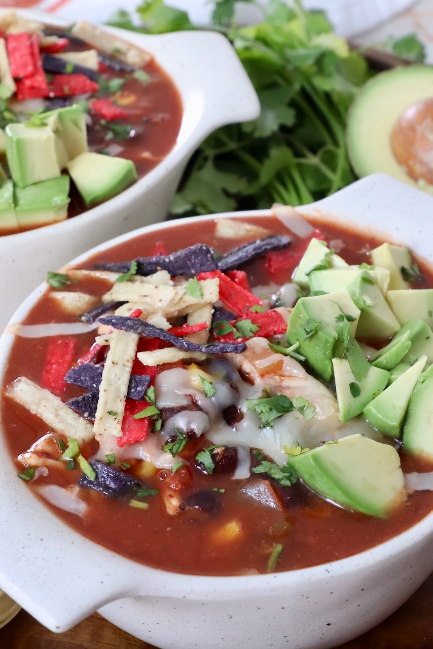 soup in bowl topped with tortilla strips and diced avocado