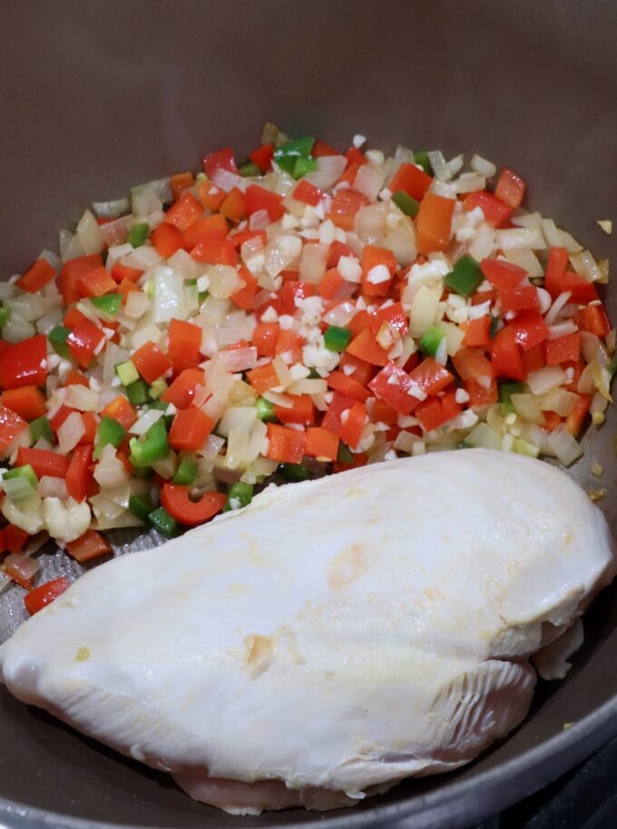 diced onion, bell pepper and jalapeno, with a seared chicken breast, in a pan on the stove